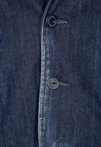 Dunkelblaue Jeansjacke mit glatter Textur, zwei schwarzen Knöpfen und einem subtilen Farbverlauf entlang der Knopfleiste und Nähte.