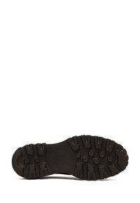 Black rubber boot sole with deep tread pattern and circular stud details for traction, shown against a white background.