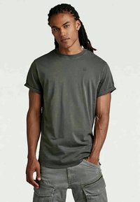 Tumehall šortsleeve T-särk ümarate varrukateotste ja kergete pahklõpsudega, valmistatud pehmest puuvillakuvast, esitades rinna peal diskreetset logo.