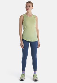 Top sin mangas de color verde claro con una textura suave, combinado con leggings ajustados de color azul y zapatillas deportivas multicolores.