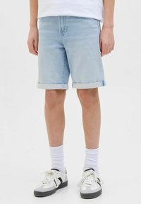 Shorts in denim azzurro con orli arrotolati, cinque tasche e vestibilità rilassata. Abbinati a calzini bianchi e sneakers con dettagli neri.