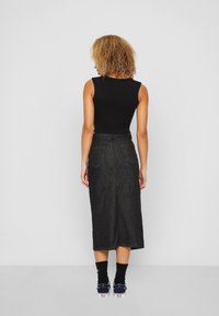 Schwarzes ärmelloses Oberteil mit hohem Kragen, kombiniert mit einem dunklen Jeans-Midi-Rock und marineblauen Sneakers, das eine taillierte Silhouette und minimalistisches Design zeigt.