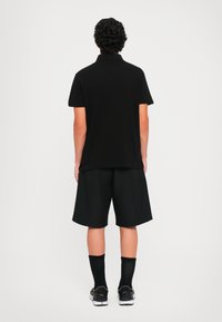 Polo negru cu mâneci scurte, asociat cu șorturi negre până la genunchi. Completat cu șosete negre și adidași. Design minimalist.