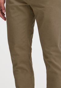 Pantalones de algodón caqui con un corte Slim, que presentan una textura suave y detalles cosidos a lo largo de las costuras laterales.