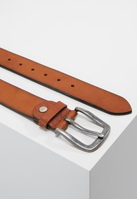 Bruine leren riem met een zilveren metalen gesp, voorzien van duidelijke perforaties en een textuur lus, liggend op een vlakke ondergrond.