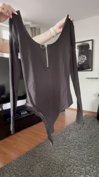 Musta pitkähihainen bodysuit, jossa on avonainen kaula-aukko ja etuvetoketju, sileä pinta ja tiukka istuvuus, kapeneva alhaalta.