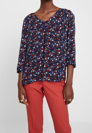 Blusa floreale con sfondo blu navy, caratterizzata da accenti rossi, blu e bianchi. Scollatura a V e maniche a tre quarti. Tessuto leggero.