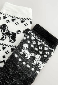 Zwei Paare gestrickte Socken in kontrastierenden Farben: eine weiße mit schwarzen Hundemustern und eine schwarze mit weißen Hundedesigns und Herzen.