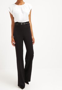 Witte blouse met korte mouwen en een geplooide halslijn, gecombineerd met high-waisted zwarte broek met een dunne riem en een uitlopende pijp.