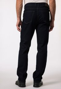 Granatowe dżinsy o prostym kroju nogawki, z dwiema tylnymi kieszeniami i subtelnymi detalami stebnowania. Noszone z czarnymi butami.