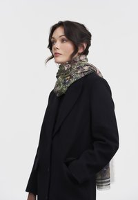 Manteau en laine mélangée noir avec une finition texturée, associé à une écharpe multicolore à motifs floraux et bords frangés.