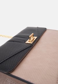 Czarna i beżowa torebka o fakturowanej powierzchni, złotych elementach i łańcuszkowym pasku. Zapięcie to prostokątna, metalowa zatrzaska.