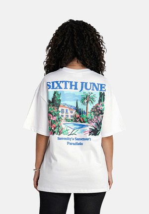 Witte oversized t-shirt met een kleurrafische afbeelding van een huis, palmbomen en bloemaccenten op de achterkant. Text leest "SIXTH JUNE."