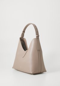 Sac à épaule en cuir beige avec une silhouette courbée, une sangle réglable et un logo doré sur le devant. Texture lisse et structurée.