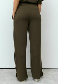 Olive green wide-leg pants with side pockets, white side stripes, and a soft texture. Cut with a relaxed fit and ankle slits.