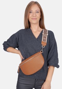 Braune Leder-Crossbody-Tasche mit runder Form, strukturierten Oberflächen und einem gemusterten, verstellbaren Tragegurt in erdigen Tönen und geometrischen Designs.
