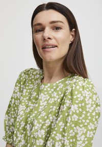 Robe florale verte en tissu texturé avec des motifs de fleurs blanches, encolure ronde et manches froncées.