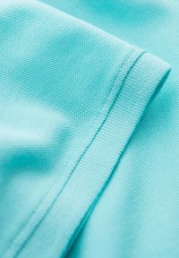 Tyrkysová tkanina s texturovaným vazebním vzorem, s hladkým okrajem a plochými švy. Materiál vypadá měkký a lehký.
