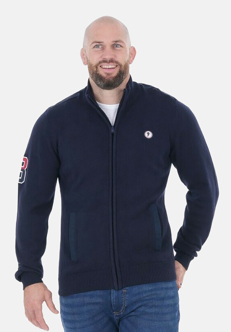 Cardigan zippé marine en tissu texturé, avec poches latérales et un patch logo sur la poitrine gauche. Coupe classique avec des poignets côtelés.