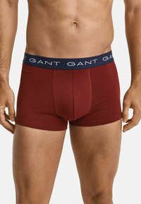 Bordeauxfarbene Boxershorts mit einem marineblauen Bund, der ein sich wiederholendes weißes "GANT"-Logo zeigt. Glattes Material mit einer figurbetonten Passform und einer Länge bis zur Mitte des Oberschenkels.