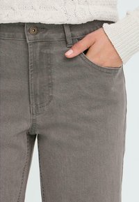 Pantalones de mezclilla grises con un acabado texturizado, que cuentan con un bolsillo frontal y un cierre de botón visible en la cintura.