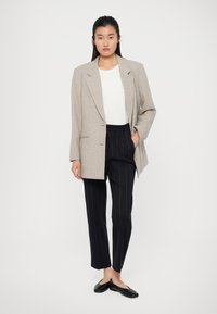 Light grey oversized blazer with structured shoulders, worn over a white top and black pinstripe pants, completed with black flats.