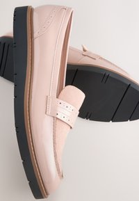 Mocassins en cuir verni rose clair avec semelles en caoutchouc noir épaisses et bride perforée décorative sur le dessus.