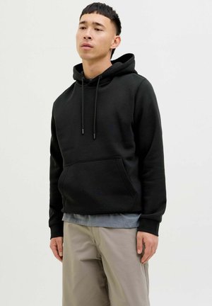 Black hoodie with a kangaroo pocket, drawstring hood, and ribbed cuffs. Paired with gray layered shirt and beige pants. Smooth texture.