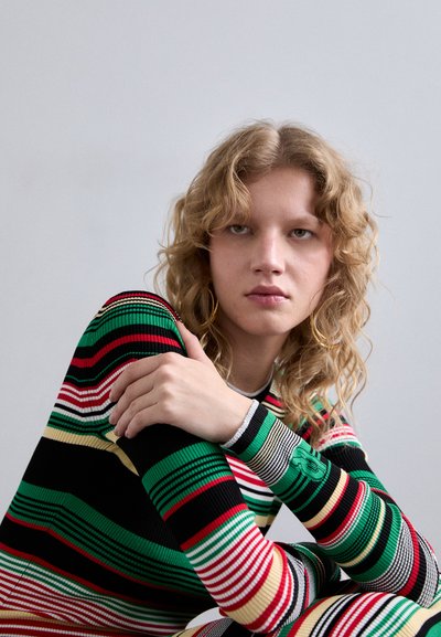 Maglione a coste con strisce orizzontali multicolori in verde, rosso, nero e beige. Maniche a tre quarti con dettaglio del logo.
