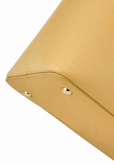 Spodnji kot bež teksturirane usnjene torbice z vidnim šivanjem in dvema kovinskima zaščitnima zatičema.