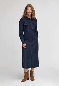 Denim midi-klänning med långa ärmar, spetsig krage, bröstfickor, vertikal sömnad och en mörk tvätt; i kombination med beige mocka ankle boots.