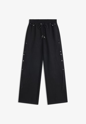 Pantalones negros de pierna ancha con cintura elástica y cordones, con cordones decorativos y herrajes plateados a lo largo de las piernas.
