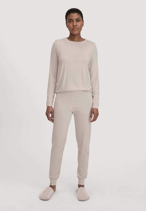 Helles beiges Loungewear-Set aus weichem Material, bestehend aus einem Langarm-Top und einer Hose mit elastischem Bund und Knopfdetails, kombiniert mit kuscheligen Hausschuhen.