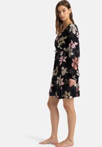 Black floral dress with long sleeves, featuring pink and cream flower patterns, a fitted waist, and a relaxed skirt. Soft fabric, lightweight texture.