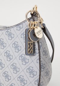 Light gray synthetic handbag with embossed logo pattern, gold hardware, short handle, and attached charm tags. Smooth texture, curved shape.