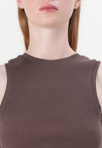 Brown ribbed tank top with a high neckline and sleeveless design, made from a stretchy material, highlighting a smooth texture.