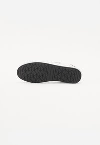 Baskets blanches avec une semelle noire en caoutchouc présentant un motif de semelle en diamant. Le matériau supérieur semble lisse avec des accents minimes.