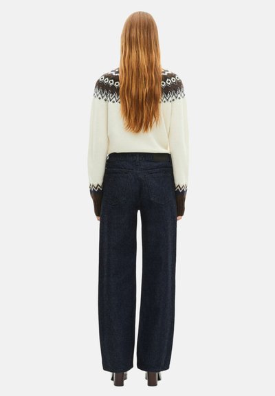 Suéter de malha creme com um yoke escuro estampado, combinado com jeans de perna larga de cintura alta azul escuro e botas de salto.
