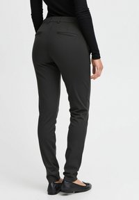 Pantaloni neri su misura con una texture liscia, vestibilità slim e due tasche posteriori. Abbinati a scarpe nere basse, visti da dietro.