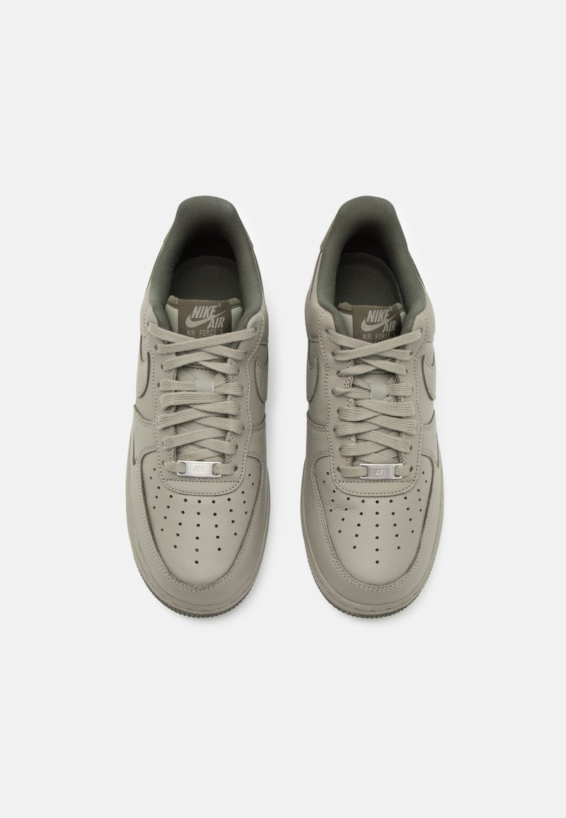 Zapatillas Nike Air Force 1 en un color gris-verde apagado, con cuero suave, puntera perforada y cordones tonales. Diseño simple con el logo de la marca.