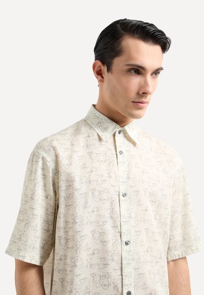 Camicia a maniche corte con colletto in un leggero crema, con un sottile motivo floreale e logo. Dotata di bottoni blu e una vestibilità comoda.