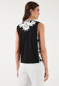 Mouwloze zwarte top met witte bloemenborduursels op de achterkant en zijkanten, met een normale pasvorm en een gladde stofstructuur.
