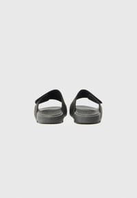 Sorte åpen-tå sandal med glatt tekstur, justerbar stropp og polstret såle. Minimalistisk design, flat silhuett og ensfarget.