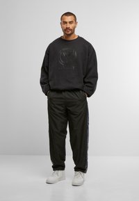 Felpa nera con logo in rilievo, abbinata a pantaloni neri con striscia laterale e sneakers bianche. Fit semplice e rilassato.