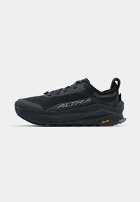 Chaussure de course noire avec un dessus texturé, un amorti léger, une semelle extérieure Vibram visible et un logo proéminent sur le côté.