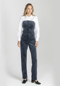 Granatowy kombinezon z korduroyu z białą koszulą z kołnierzykiem. Posiada dopasowaną górę z guzikami, zwężane nogawki oraz podwójne kieszenie w talii.