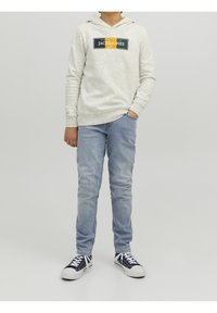 Světlě šedá mikina s logem, dlouhými rukávy a klokaní kapsou, zkombinovaná se světle modrými džíny a námořnickými teniskami s bílou podešví.