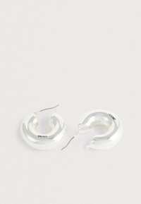 Srebrne naušnice u obliku obruča s glatkim, sjajnim finišom. Dizajn prikazuje kružni, spiralni oblik. Na jednoj naušnici vidljiv je brend.