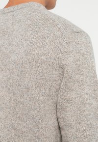 Textured gray knit sweater with a round neck, featuring a subtle blend of light gray and beige tones, showcasing a comfortable fit.