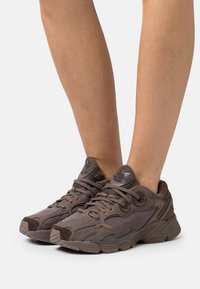 Brown mesh sneakers featuring a textured design, contrasting dark accents, padded collar, and lace-up closure.